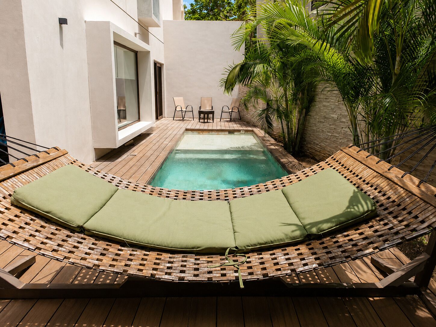 A pool area with a hammock lounge, wooden deck, and a small table with chairs.