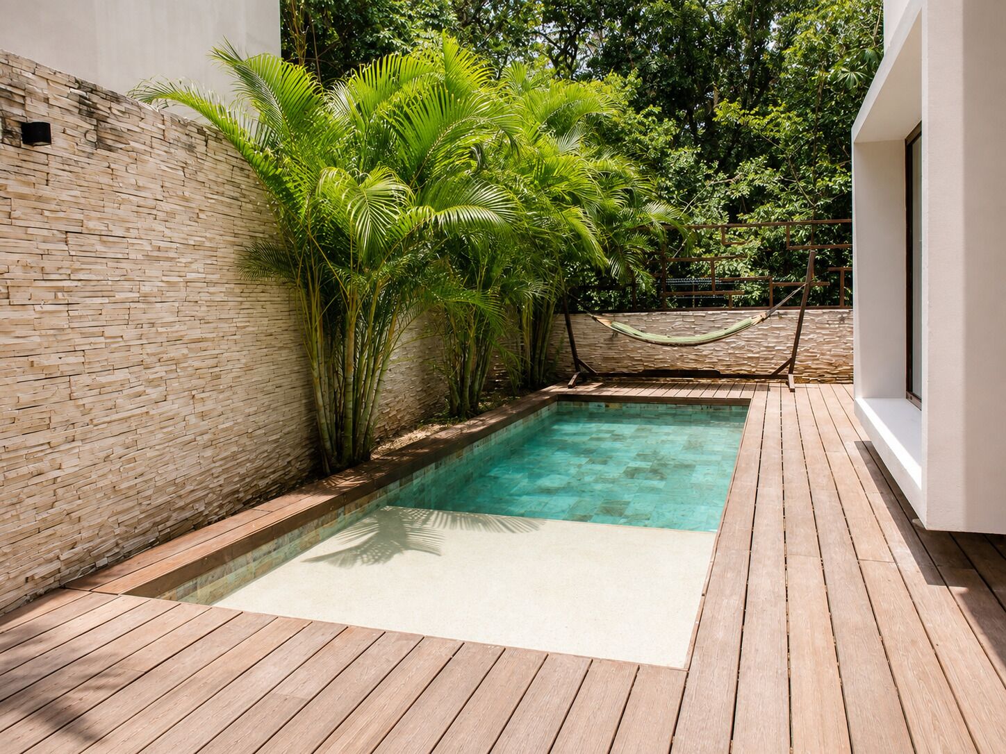 Una piscina con muelle de madera, rodeada de un muro de piedra y abundante vegetación.