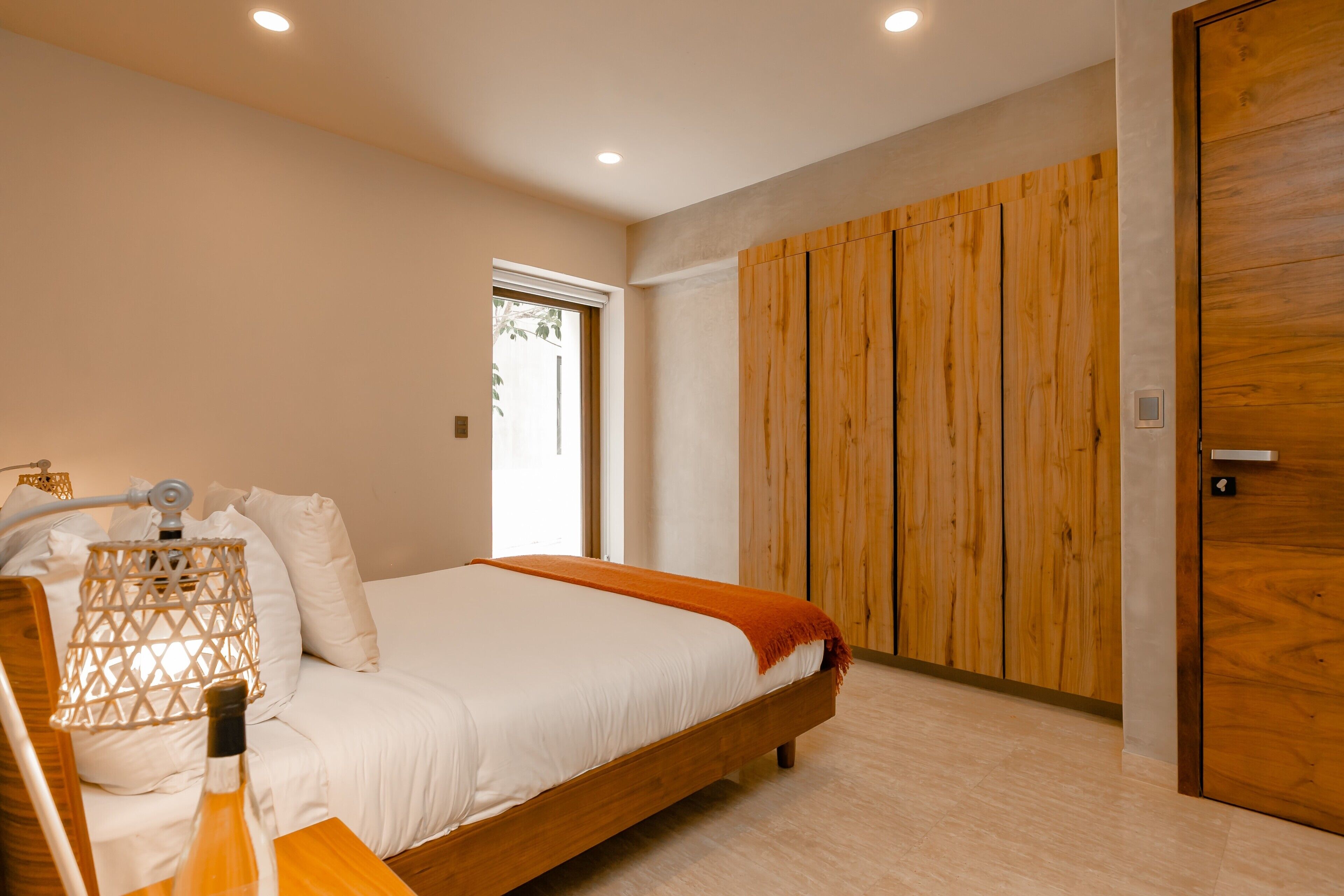 A modern bedroom with a wooden bed, white bedding, a wooden wardrobe, and a nightstand with a lamp.