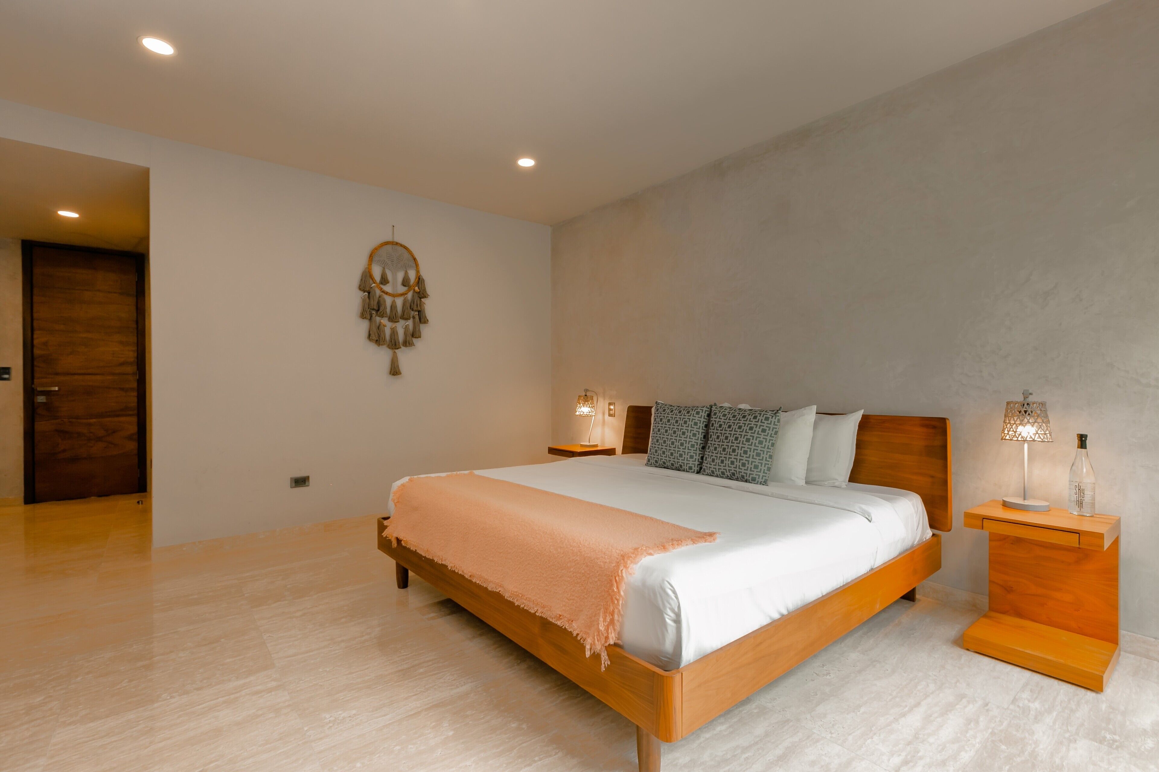 A modern bedroom with a wooden bed, a nightstand with a lamp, and a wall-mounted dreamcatcher.