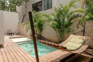 Un área de piscina con terraza de madera, una hamaca y una zona de estar con sillas y una mesa.