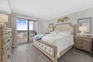Un dormitorio con una cama grande, un aparador, una mesita de noche, un balcón con cortinas y vistas a la ciudad.