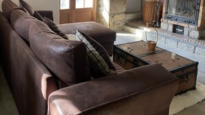 Een gezellige woonkamer met een stenen open haard, een leren bank en een rustiek houten plafond.