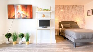 Een moderne slaapkamer met een bed, een televisie bevestigd aan een witte plank, en een afbeelding van een open haard aan de muur.