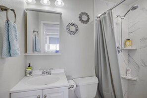 Ein Badezimmer mit weißem Waschbecken, Toilette und Duschvorhang. Über dem Waschbecken befinden sich dekorative Wandspiegel und ein Seifenspender.