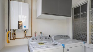 A laundry area with a white washer and dryer, a water heater, and a window with a grid pattern. - Remodeled Studio w/Fast Wi-Fi in Heart of Bay Area (Milpitas)