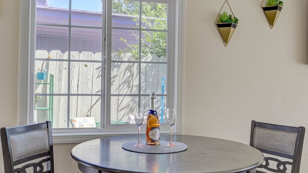 A round table with a bottle and two glasses, a window with a view of a fence and trees, and two wall-mounted planters. - Remodeled Studio w/Fast Wi-Fi in Heart of Bay Area (Milpitas)