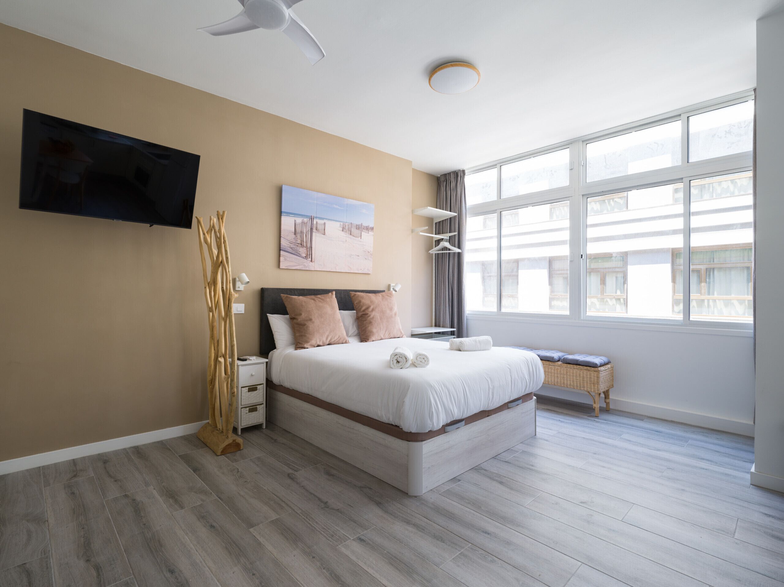 Un dormitorio moderno con una cama grande, un televisor de pantalla plana, un ventilador de techo y un ventanal amplio.