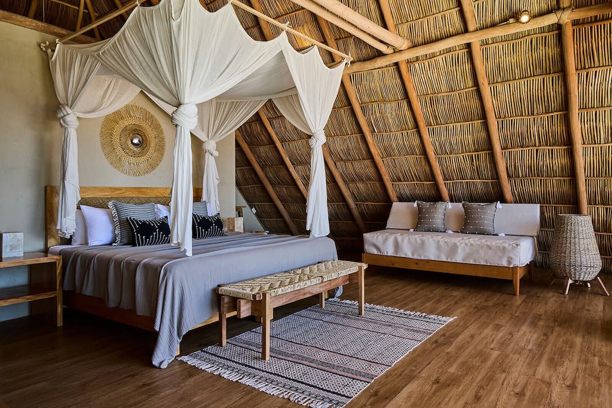 A bedroom with a four-poster bed, a sofa, a bench, and a woven basket.