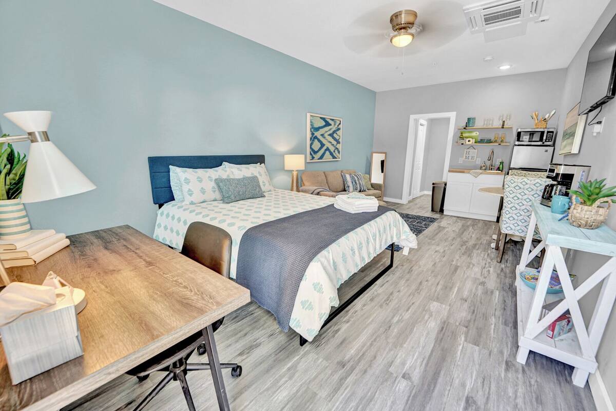 A modern bedroom with a bed, bedside tables, a desk, and a kitchenette.