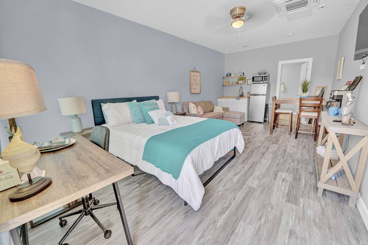 A bedroom with a bed, bedside tables, a desk, and a kitchenette.