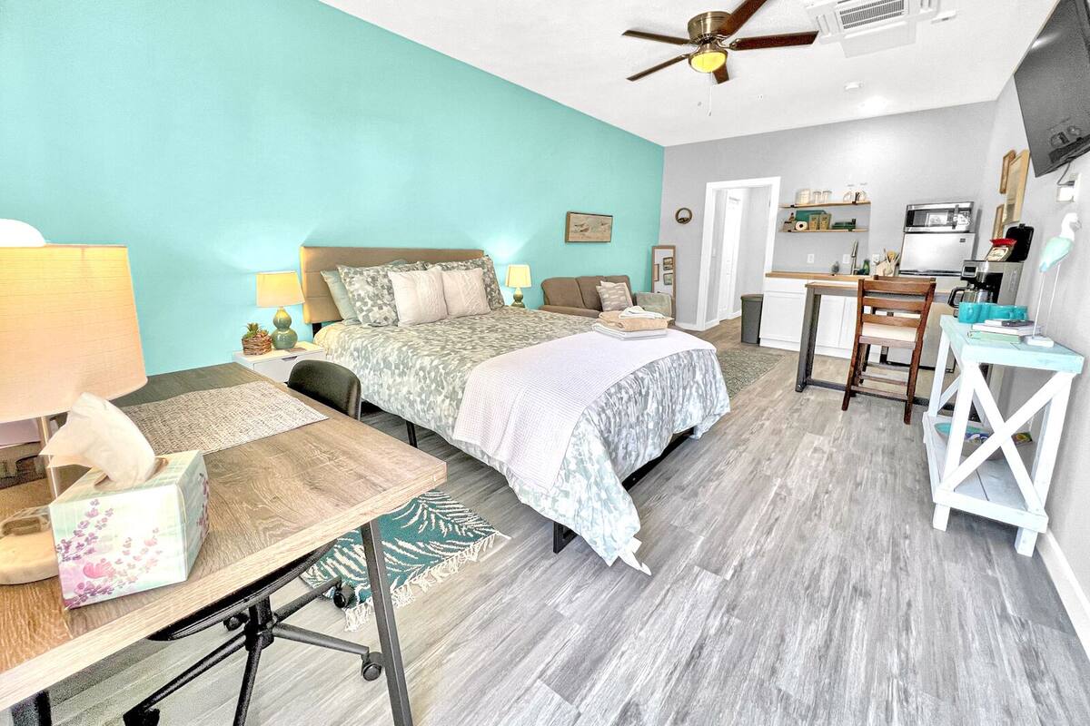 A bedroom with a bed, desk, and kitchenette.