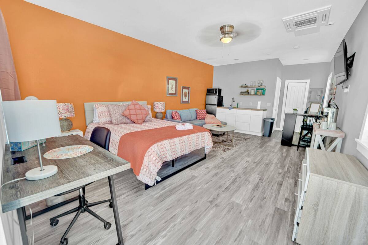 A compact bedroom with a bed, bedside tables, a desk, and a kitchenette.