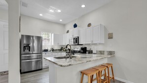 A modern kitchen with white cabinets, stainless steel appliances, a marble countertop, and wooden stools.