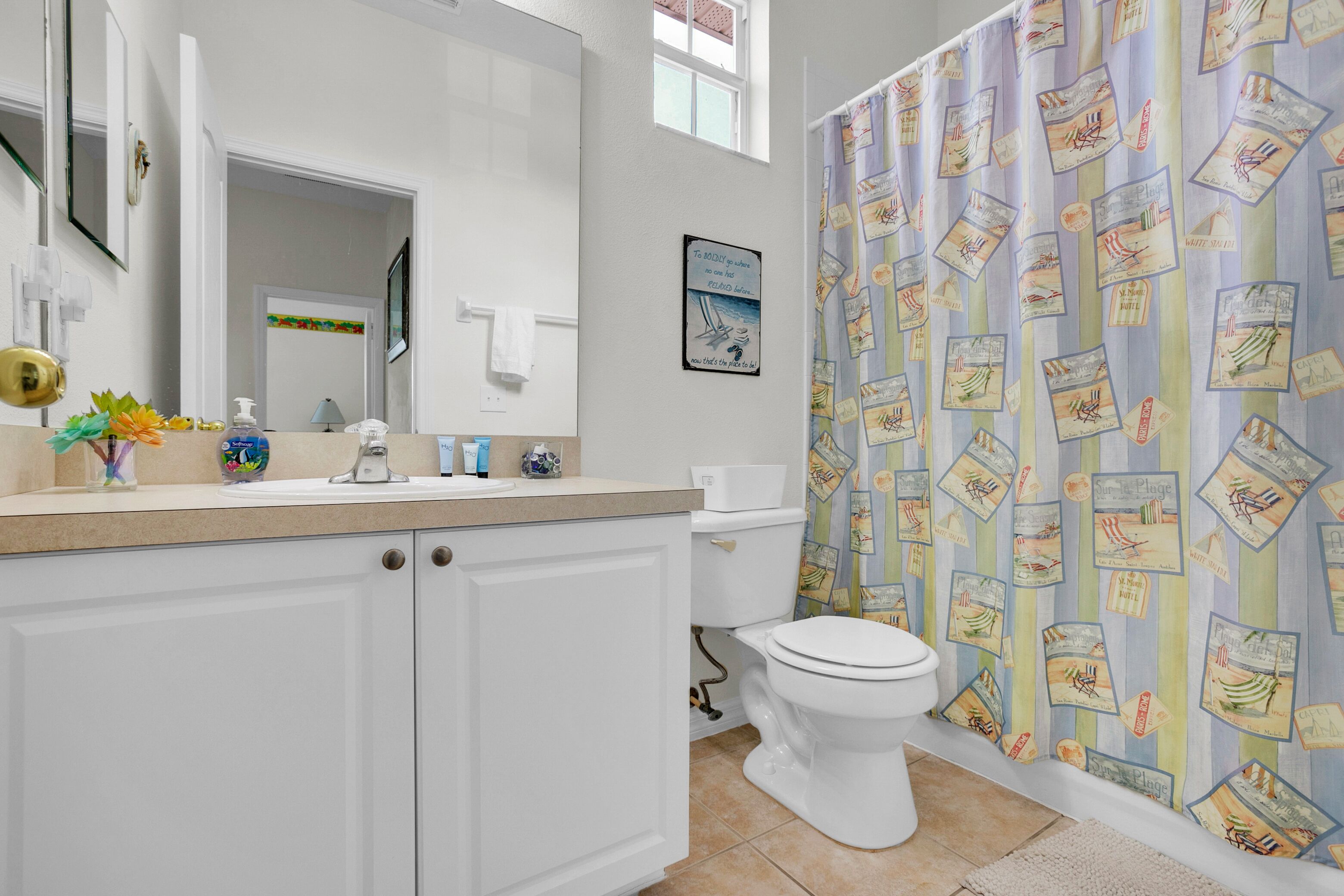 A bathroom with a white toilet, a sink with a mirror above it, and a shower curtain with travel-themed designs.