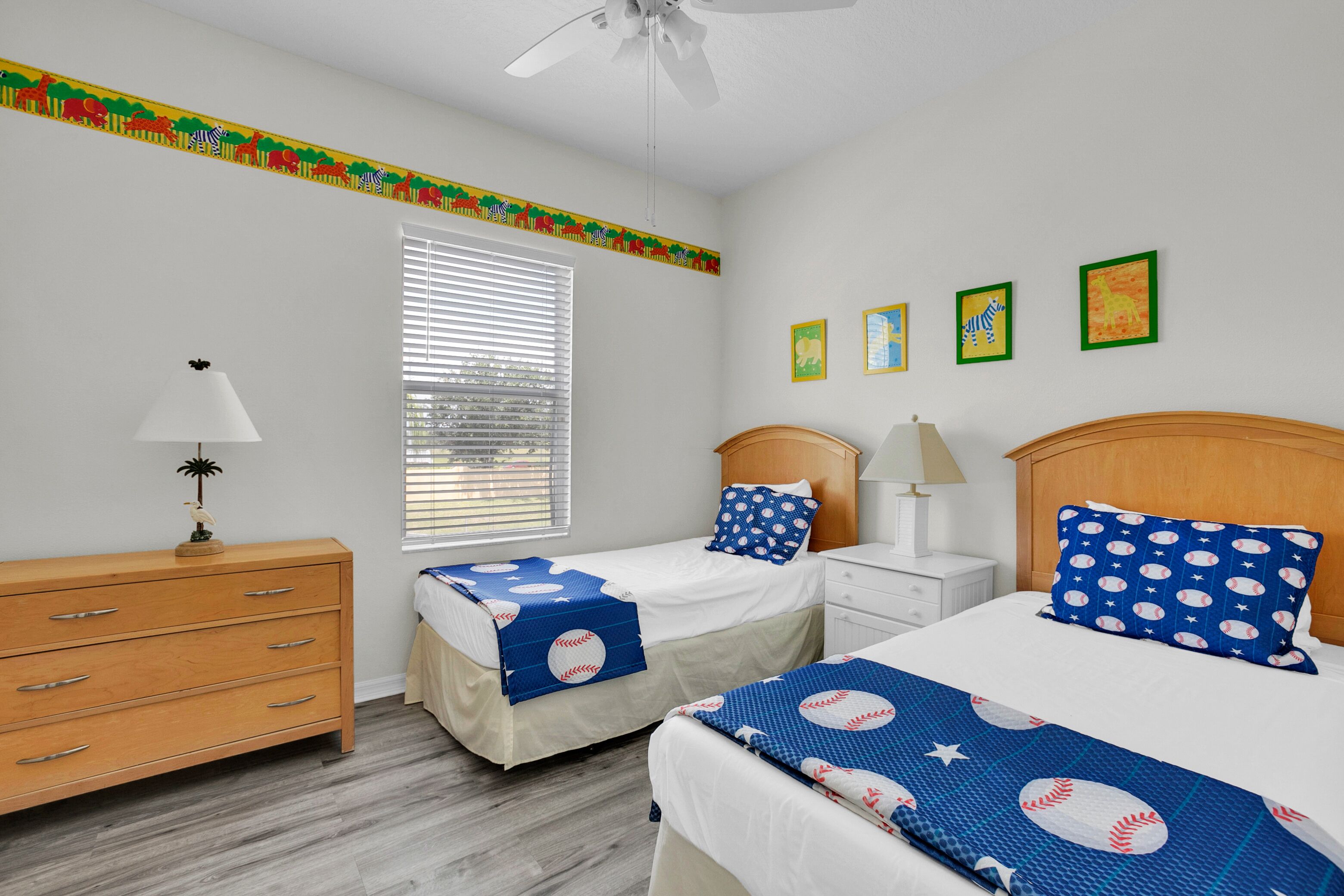 A bedroom with two beds, a dresser, a ceiling fan, and a window with blinds.