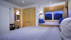 Un dormitorio con cama, ventana con vista a montañas, armario de madera y espejo.