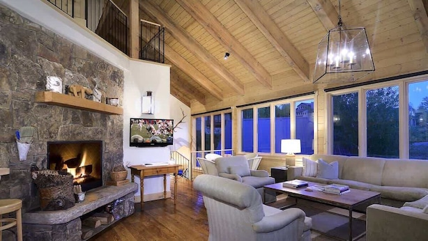 Amplia sala de estar con chimenea de piedra, vigas de madera, balcón y ventanas grandes.