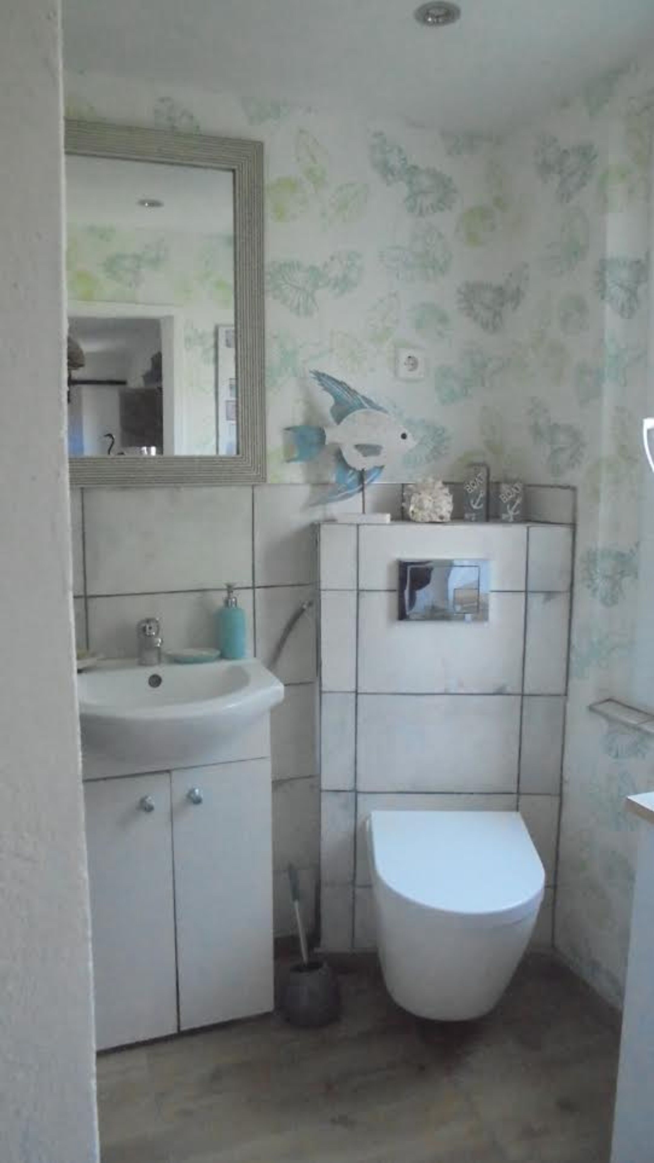 Et lille badeværelse med vask, spejl, toilet og en kost.
