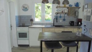 A kitchen with a wooden table, two chairs, a sink, a stove, and a window with a view of greenery. - Small oasis of peace surrounded by greenery - 3 minutes from Kromlau Rhododendron Park (Gablenz)
