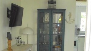 A room with a wooden dresser, a television mounted on the wall, and a glass-fronted cabinet with various items inside. - Small oasis of peace surrounded by greenery - 3 minutes from Kromlau Rhododendron Park (Gablenz)