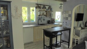 Una cocina compacta con lavamanos, cocina y lámparas colgantes. Hay un pequeño comedor con una mesa y dos taburetes.