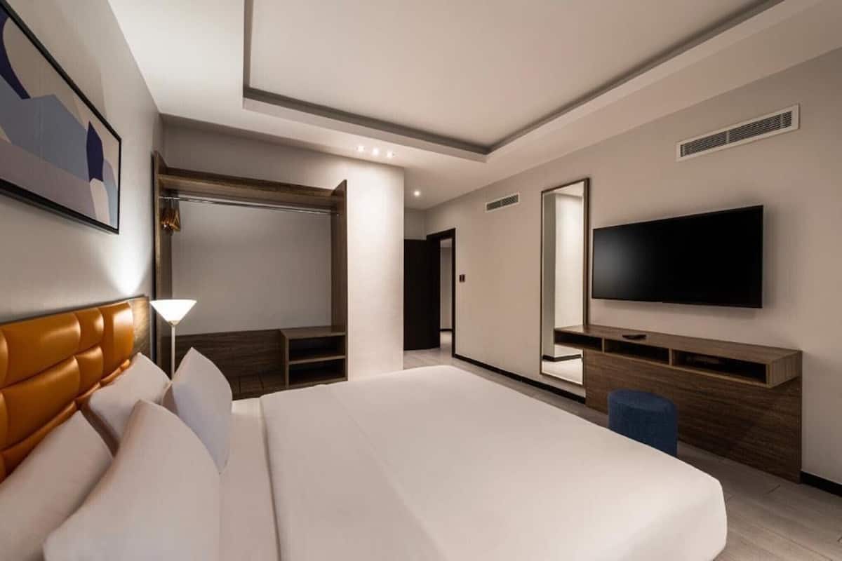 Una habitación de hotel moderna con una cama grande, televisión de pantalla plana, un escritorio y un vestidor.