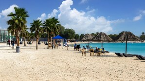Una playa con palmeras, una sombrilla azul y sillas para la playa.