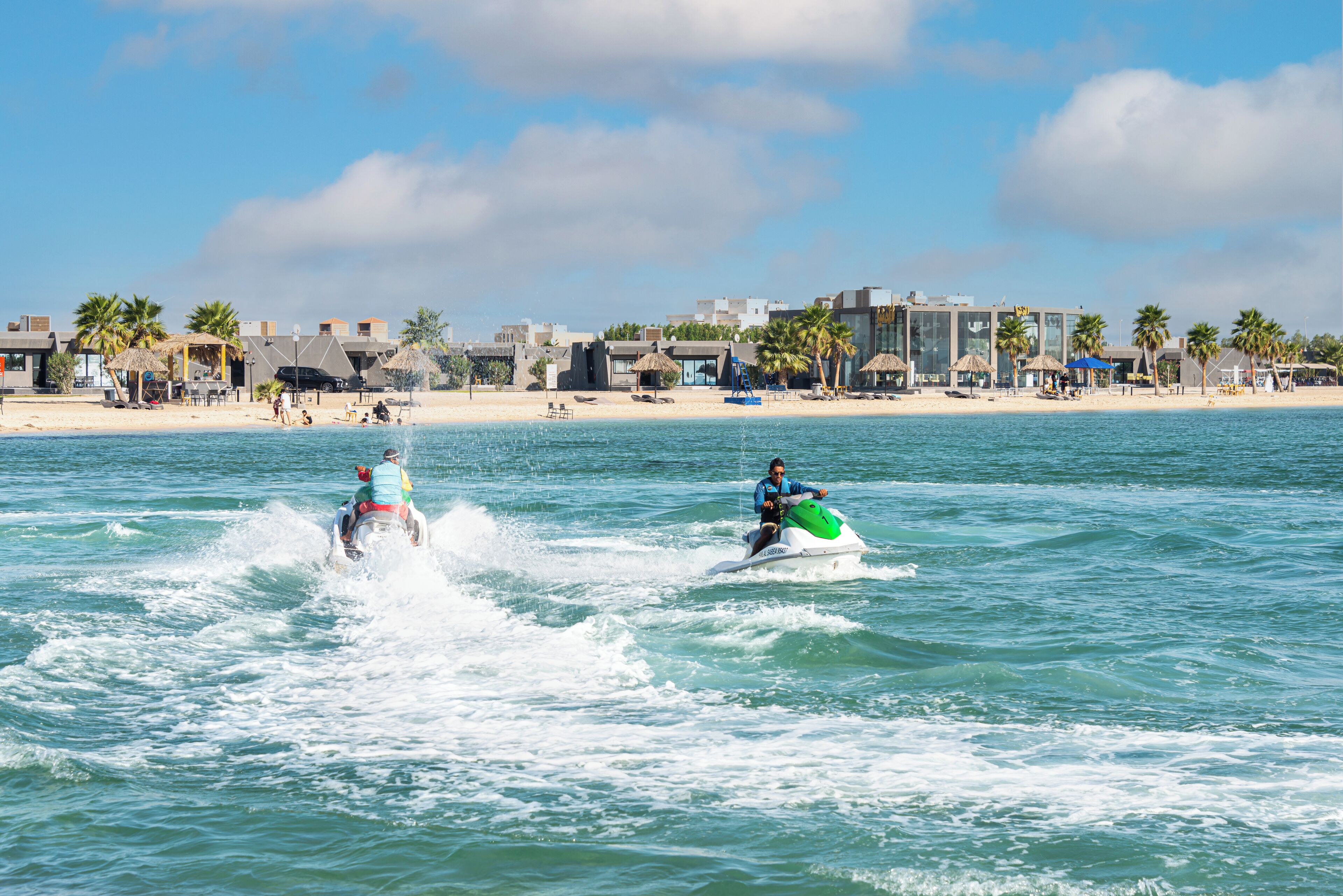 Zwei Jetskis auf ruhiger See, im Hintergrund ein Strand und Gebäude.
