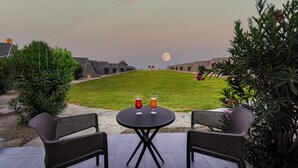 Un área de estar al aire libre con dos sillas y una mesa, la luna de fondo y un césped bien cuidado.