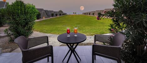 An outdoor seating area with two chairs and a table, a moon in the background, and a well-maintained lawn.