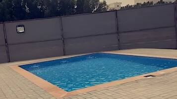 A swimming pool with a tiled deck, surrounded by a low wall and a palm tree.