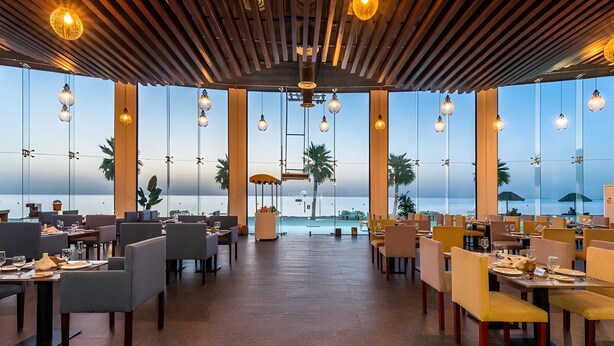 Un restaurante con vista al mar, que cuenta con techo de madera, luces colgantes y mobiliario moderno.