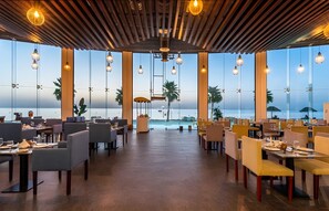 Un restaurante con vista al mar, que cuenta con techo de madera, luces colgantes y mobiliario moderno.