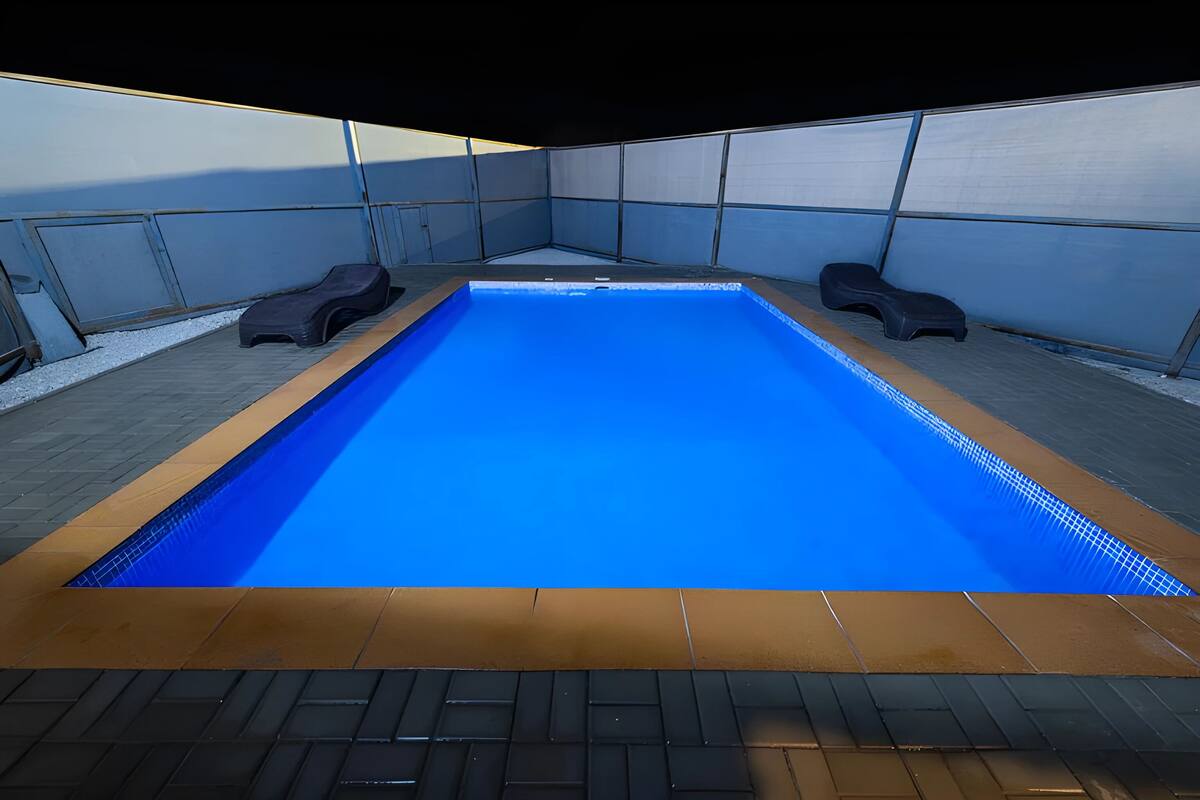 Una piscina rectangular con borde de azulejos, rodeada por una solana también de azulejos y un muro bajo con estructura metálica.