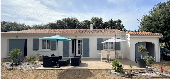 A house with a tiled roof, a patio with outdoor furniture, and a garden with various plants.