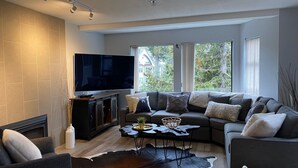 Una sala de estar moderna con un televisor de pantalla plana grande, un sofá seccional, una mesa de centro y una chimenea.