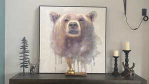 Un comedor con una mesa de madera, dos sillas, un cuadro de un oso, un jarrón y dos portavelas.