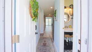 Um corredor com tapete estampado, porta com puxador de latão e planta na parede.