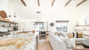 Een ruime keuken met een marmeren eiland, houten balken en een moderne hanglamp.