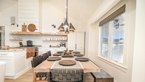 Een moderne keuken met witte kastjes, een houten eettafel, zwarte geweven stoelen en hanglampen.
