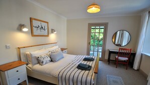 A bedroom with a bed, bedside tables, a chair, a desk, a mirror, a window, and a door. - Sea Holly Cottage- coastal retreat Pittenweem (Pittenweem)