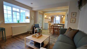 A living room with a sofa, a coffee table, and a dining area with chairs and a table. - Sea Holly Cottage- coastal retreat Pittenweem (Pittenweem)