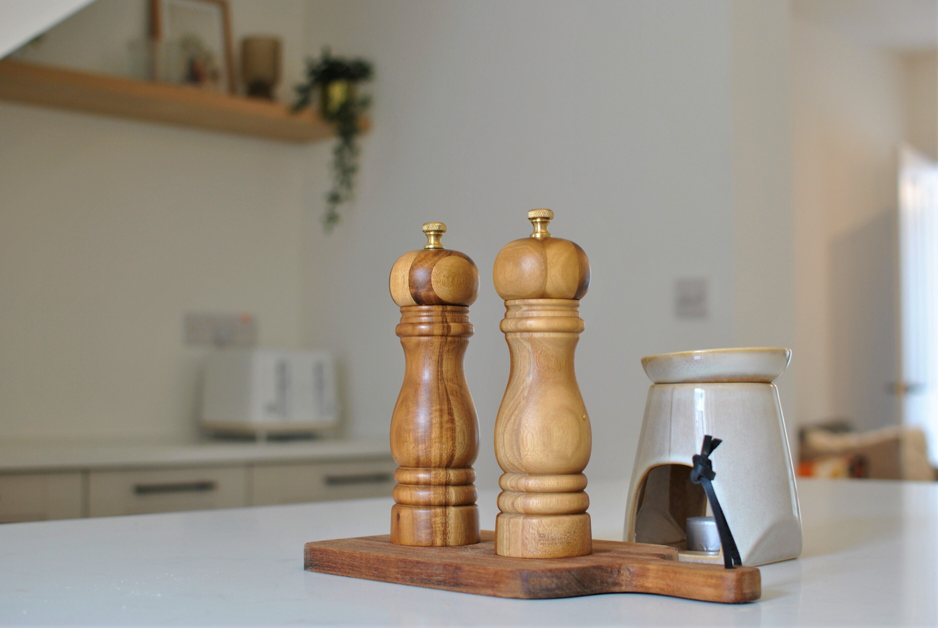 Two wooden salt and pepper shakers on a wooden board, a ceramic container with a black handle, and a kitchen counter.