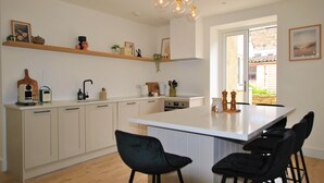 Een moderne keuken met witte kastjes, een centraal kookeiland met barstoelen en hanglampen.