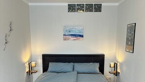 A bedroom with a bed, bedside lamps, a painting, and a wooden floor.