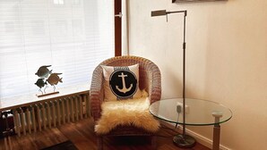A cozy room with a wicker chair, a glass table, a radiator, and a painting on the wall.
