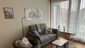 A modern living room with a grey sofa, a wooden coffee table, and a large window with sheer curtains.