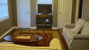 Un salon comprenant un canapé, une table basse, un téléviseur posé sur un meuble et un ventilateur de plafond.