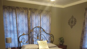 Une chambre à coucher avec un lit, une table de chevet, une lampe, une plante et un ventilateur de plafond.